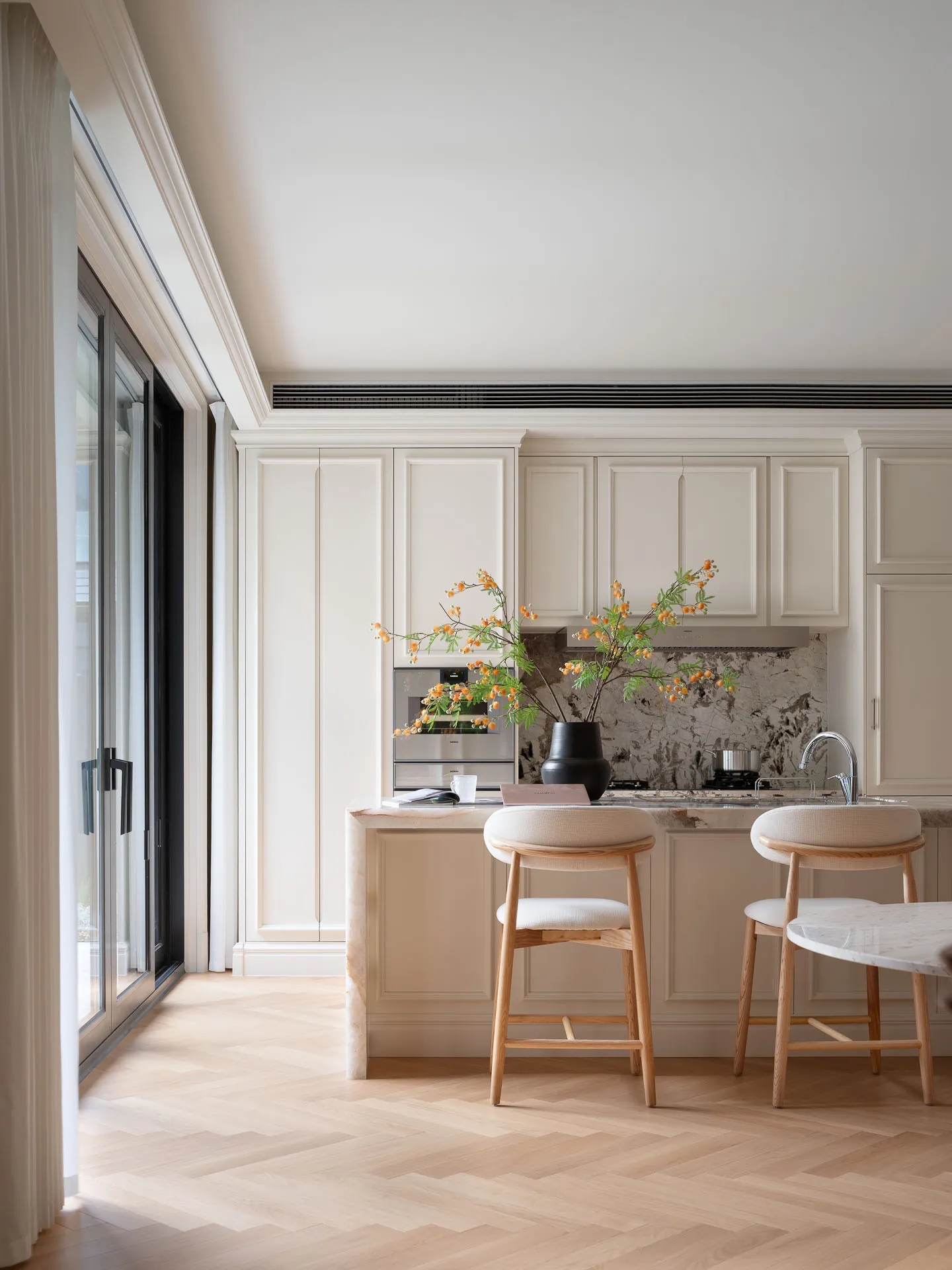 Modern kitchen with white cabinets, wooden floors, and a center island with stools, featuring a potted plant and three cups on the counter