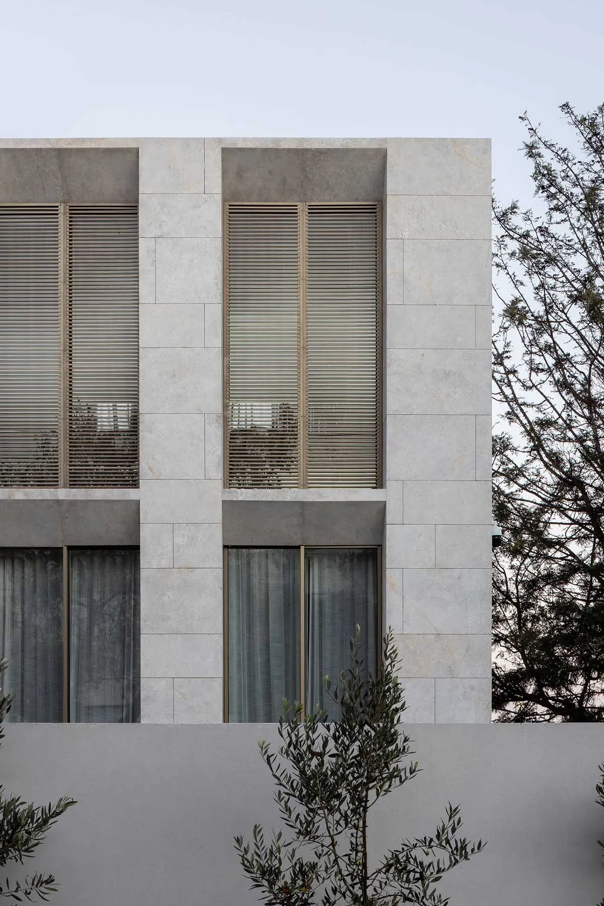 A modern building with grey stone walls and white window frames, featuring blinds and a sophisticated atmosphere