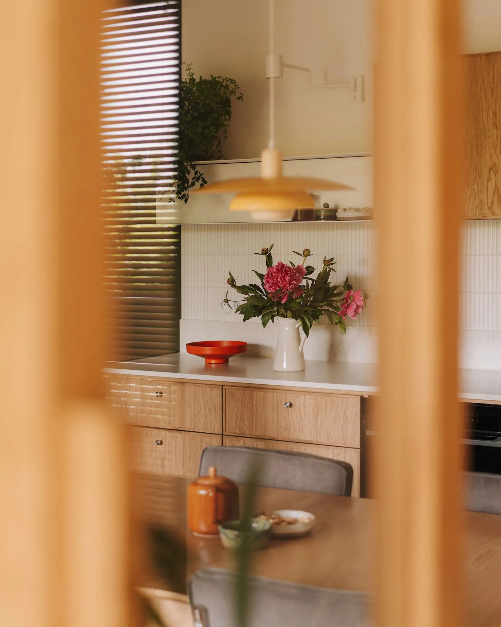 Warm kitchen with wooden cabinets and countertops, featuring a vase, bowl, cup, and potted plants, creating a cozy atmosphere