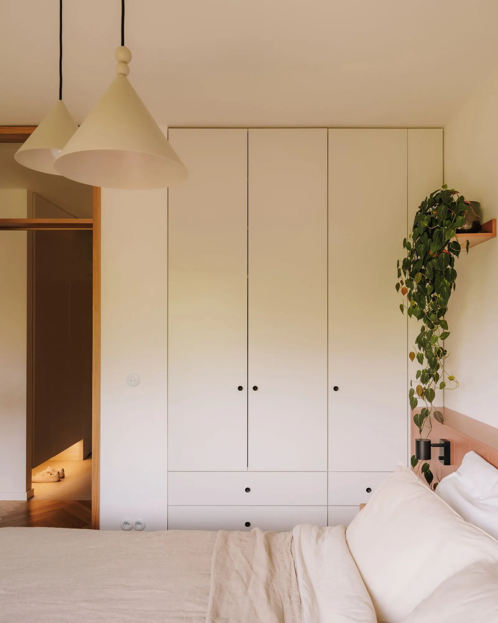 Cozy bedroom with a white bed, wooden headboard, two lamps, a closet, and a potted plant