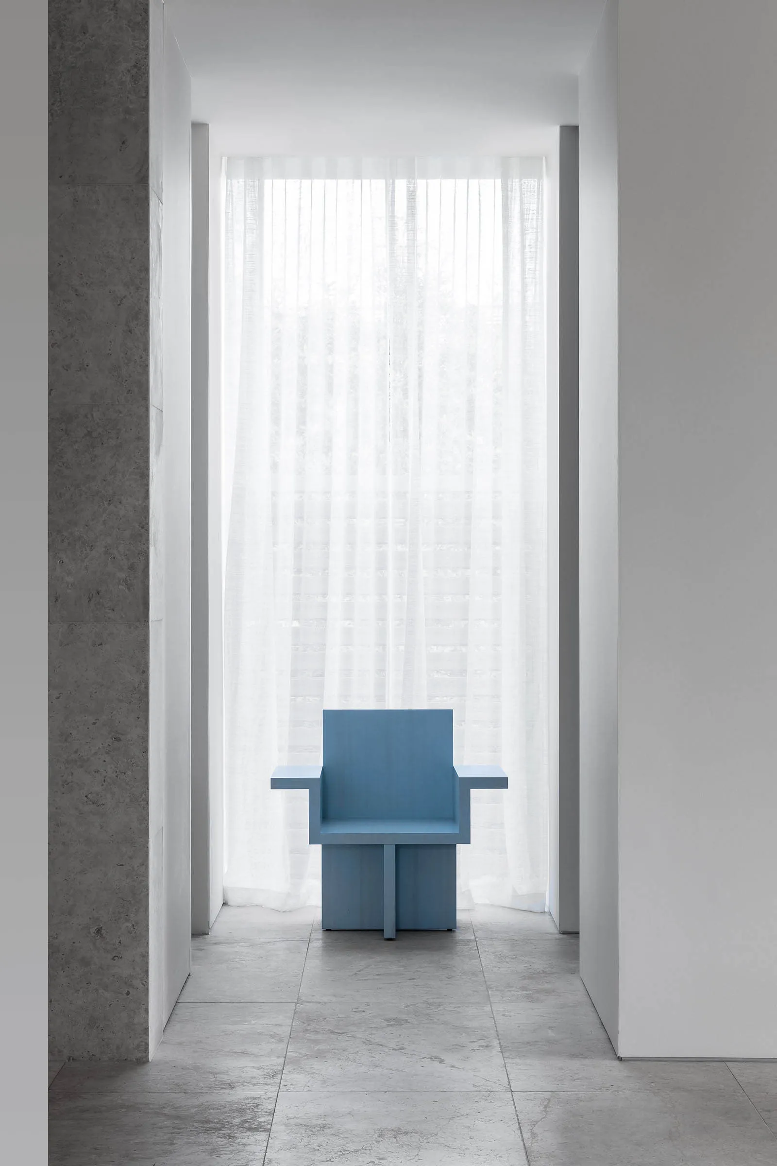 Empty room with a wooden chair and blue cushion in front of a window, surrounded by white walls and natural light