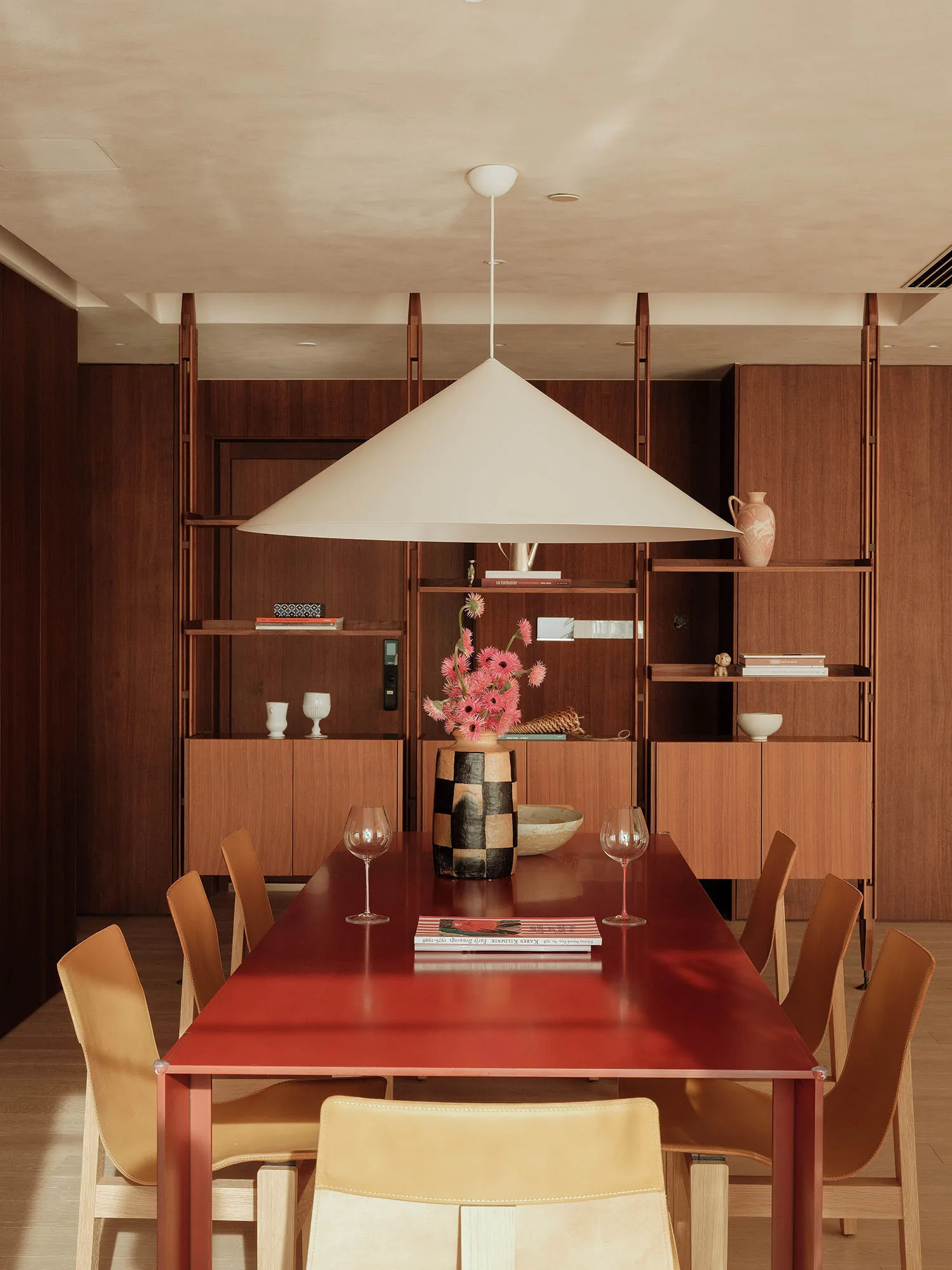 A well-lit dining area with a red table surrounded by chairs, decorated with wine glasses, bowls, and vases