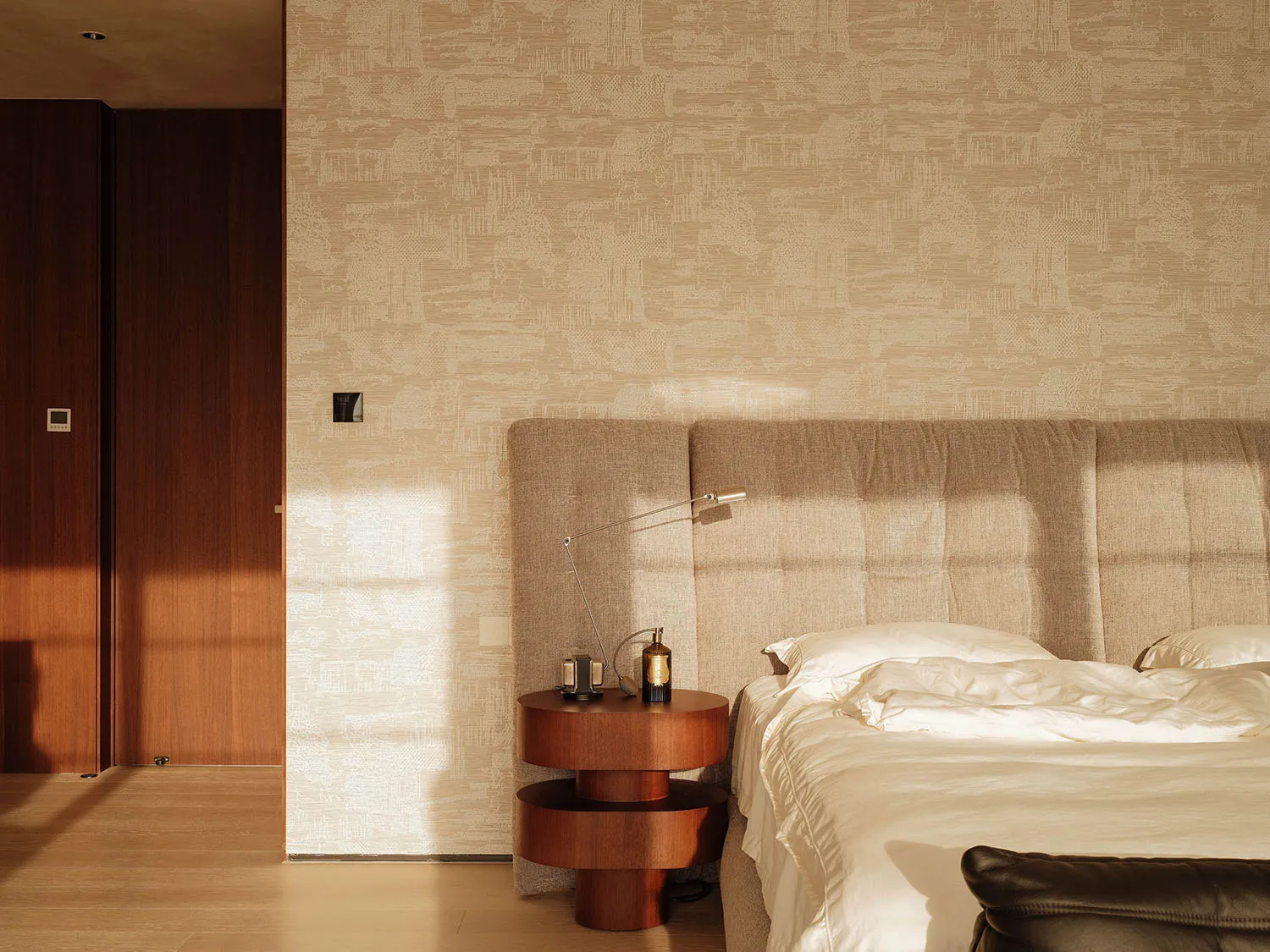 A cozy bedroom with a large bed, nightstands, a lamp, and a chair, featuring white bedding and a warm atmosphere