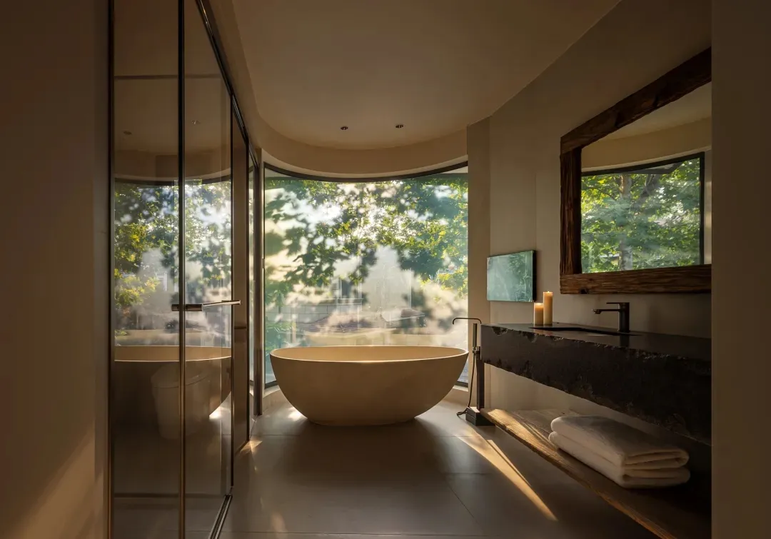 Modern bathroom with a large marble bathtub, sink, mirror, and shower area, near a window