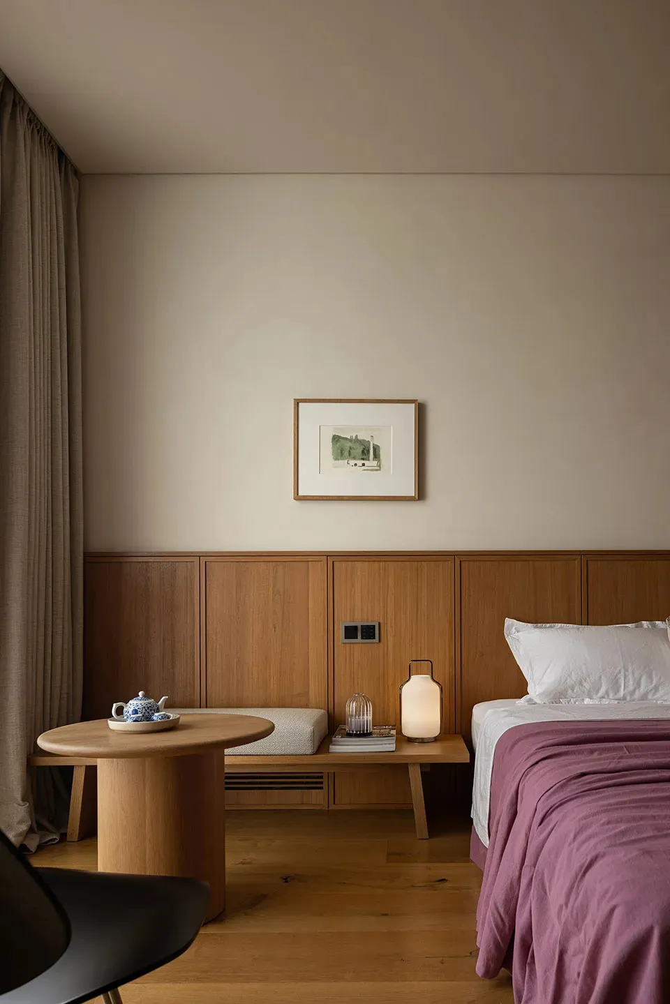 Cozy bedroom with a large bed, wooden nightstands, and a table with a bowl, illuminated by a lamp