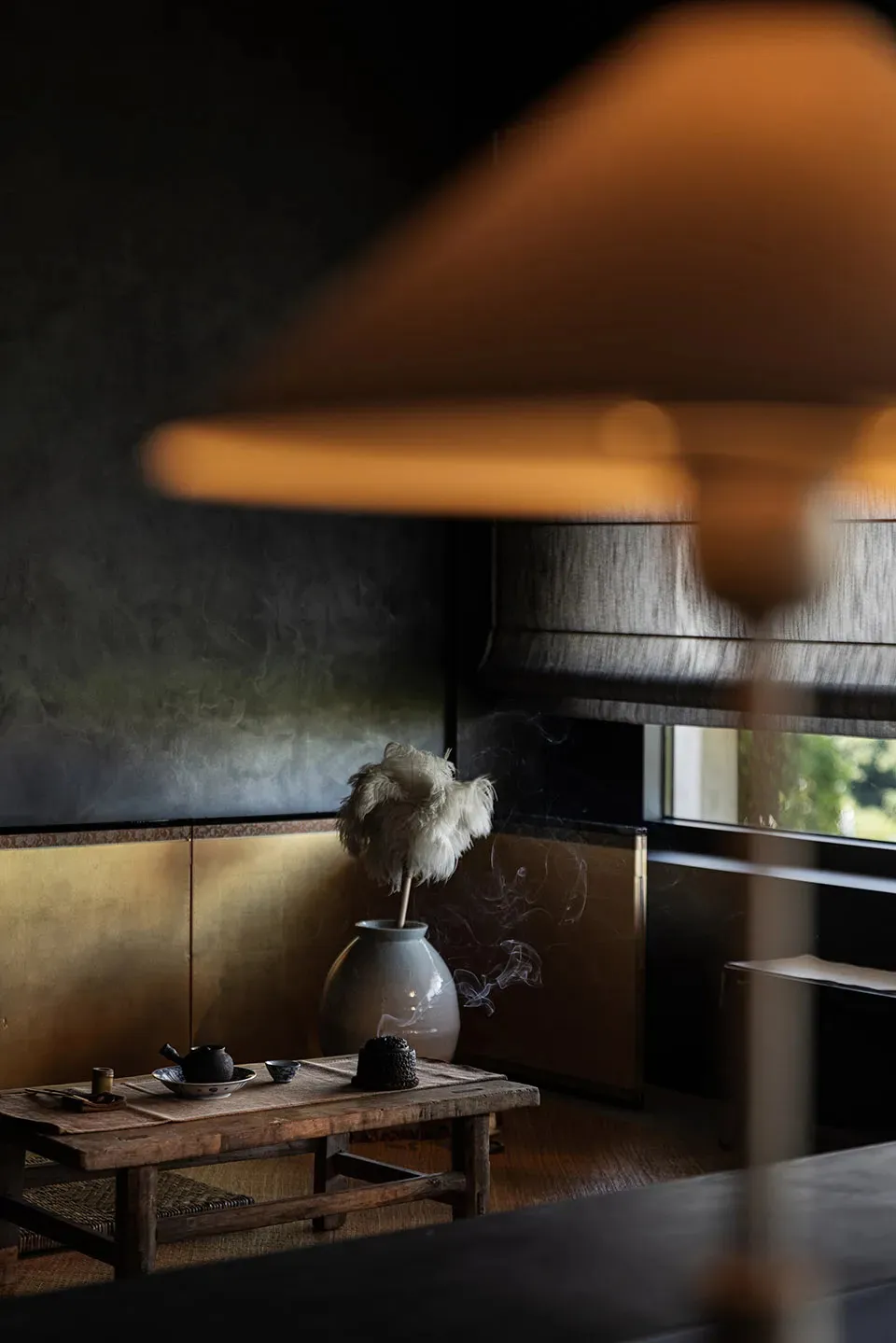 Dimly lit living area with a lamp, vase, and bowl of ashes, creating a cozy atmosphere for relaxation or reading