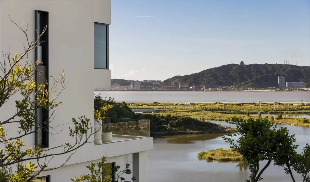 A white house situated on a hillside overlooking a large body of water, with several windows and a picturesque view from the balcony