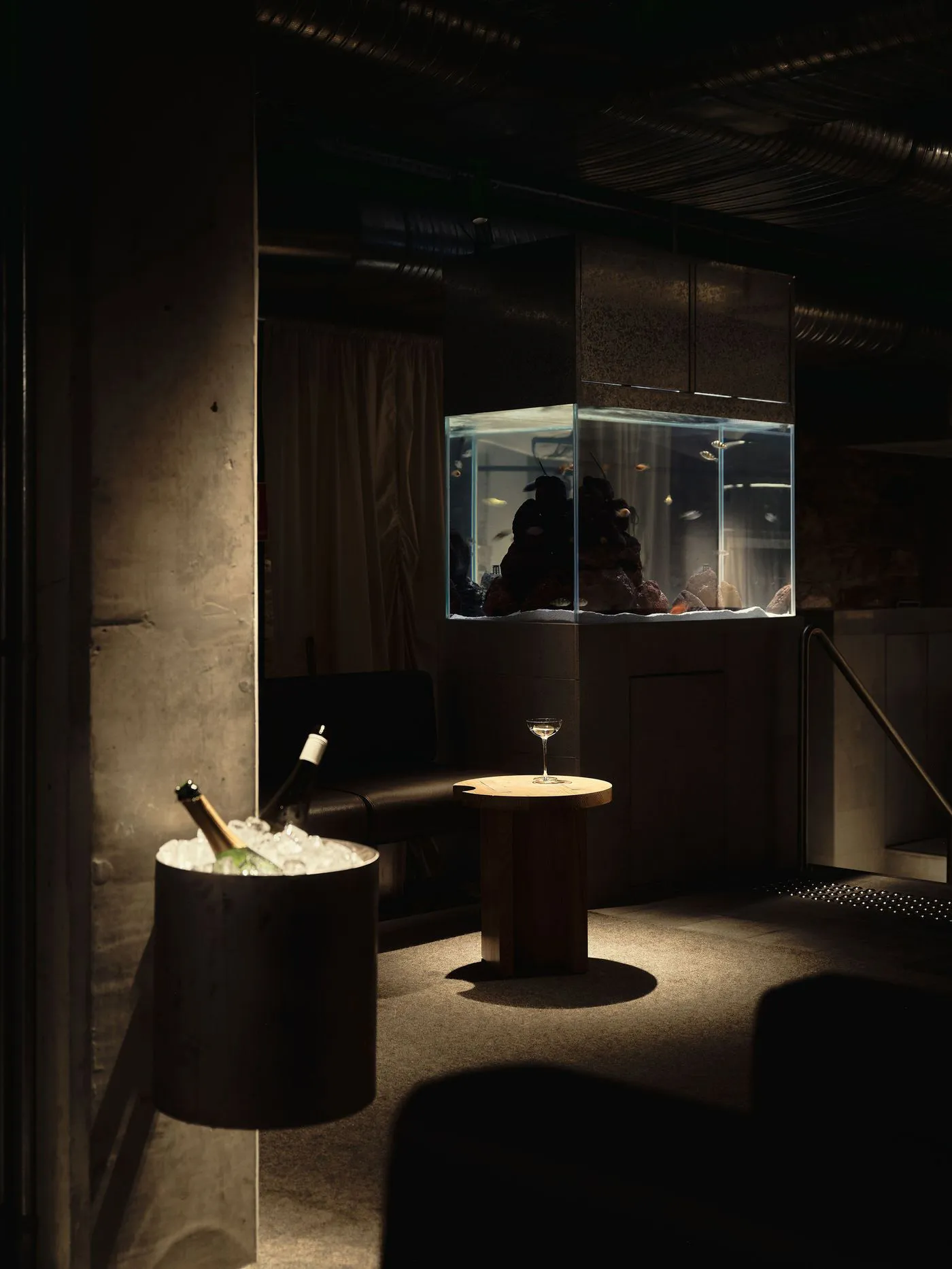Cozy living room with a large aquarium, a couch, and a dining table, featuring wood and glass materials in a dimly lit space