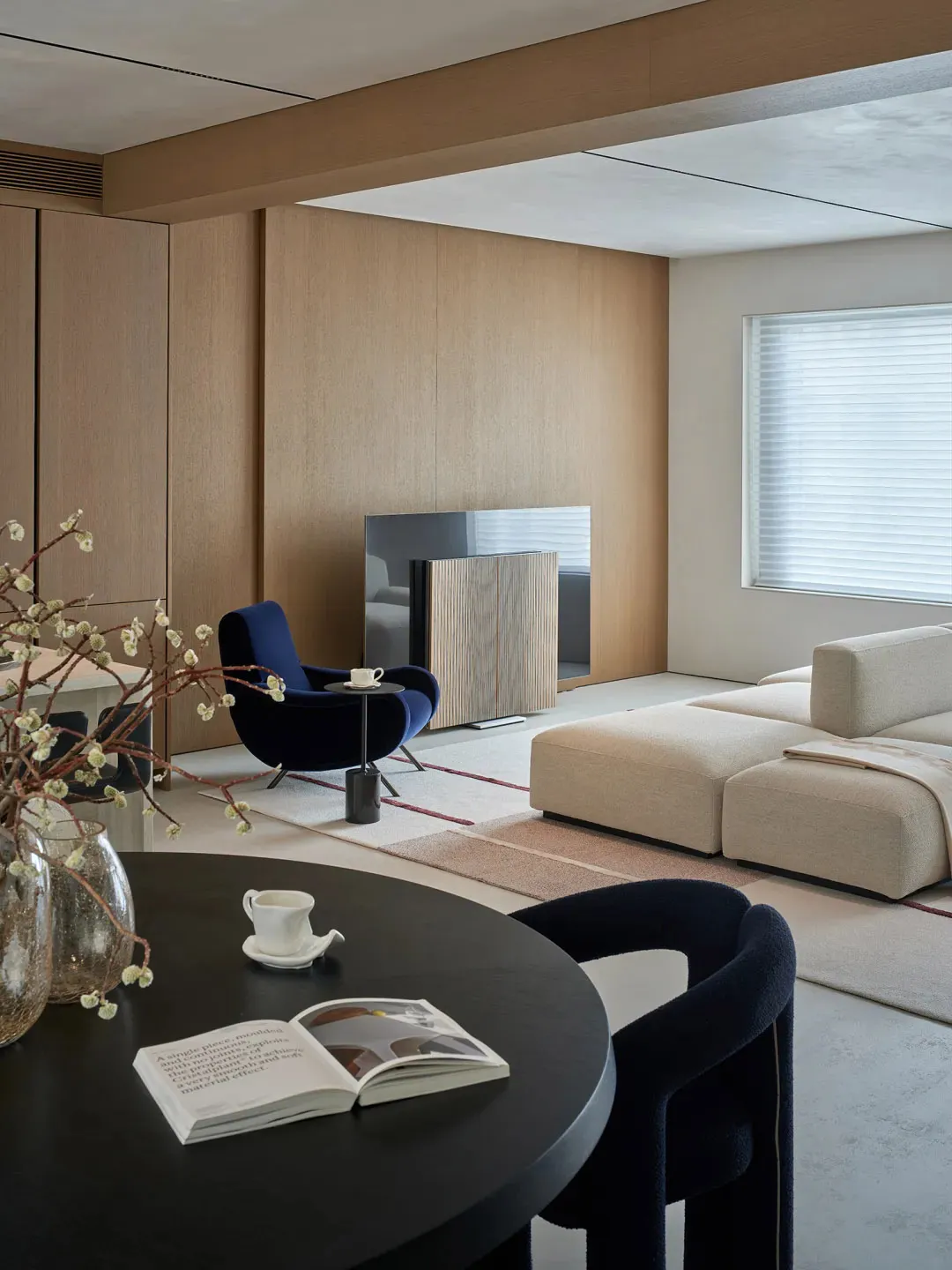Cozy modern living space with a large couch, chair, and dining table, surrounded by wooden elements and warm lighting