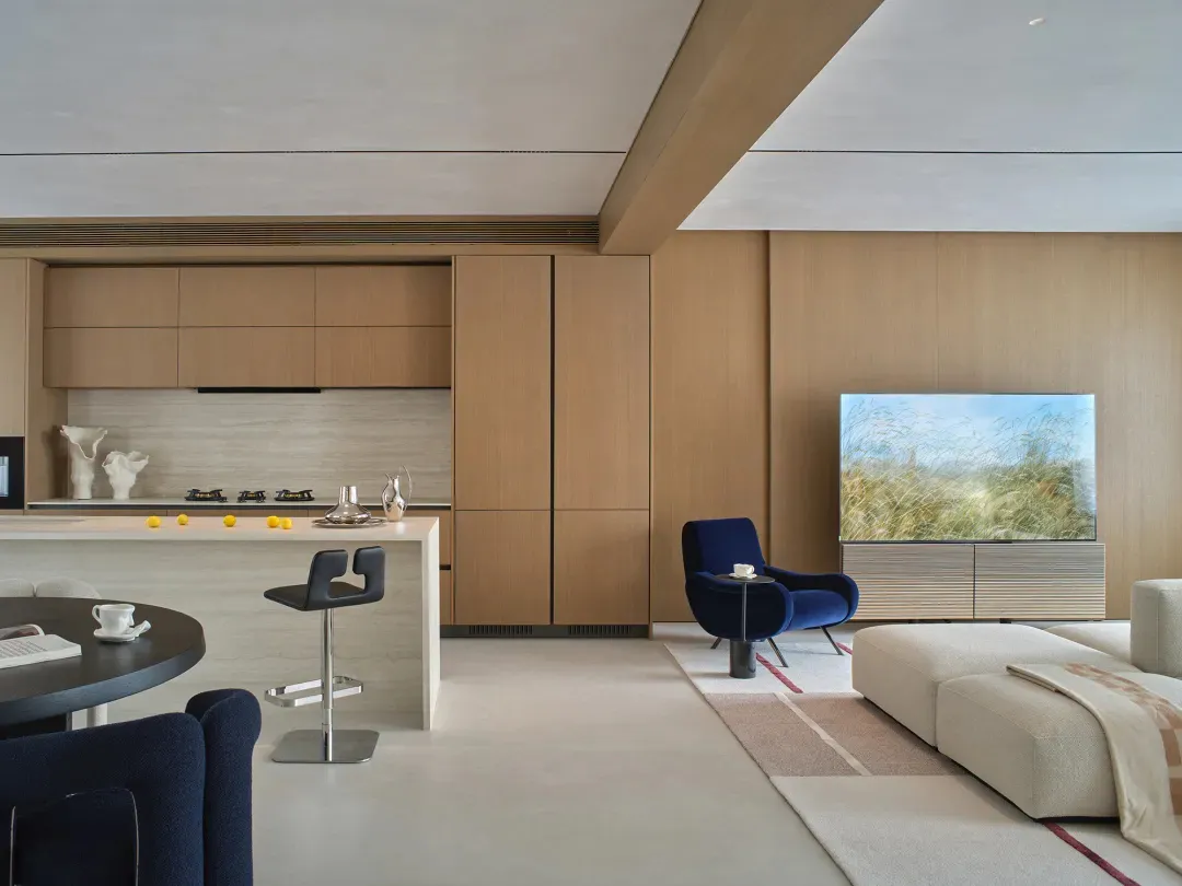 A modern living room with a large couch, chair, and dining table, decorated with wooden elements, well lit with natural light from the windows, and furnished with various items
