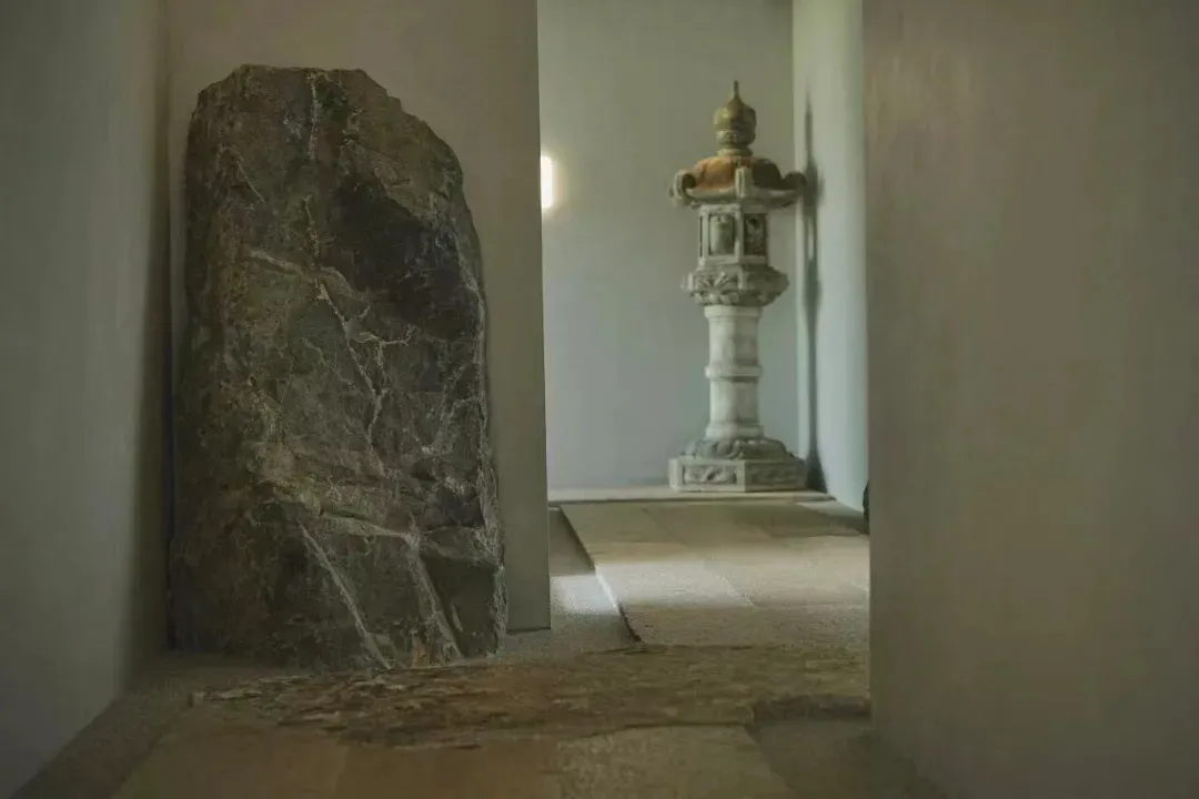 A dimly lit hallway with a stone floor, a stone pillar, and a statue, creating a solemn and quiet atmosphere