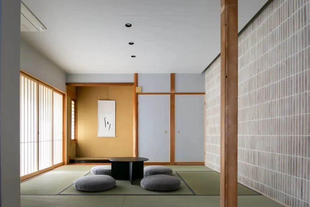 A modern dining area with a wooden floor, a tiled wall, a dining table, chairs, cushions, and a vase, creating a warm and elegant atmosphere