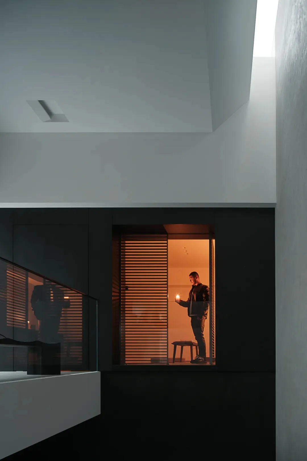 A man stands in a cozy living room with a couch and chair, lit by a candle on a surface in front of him