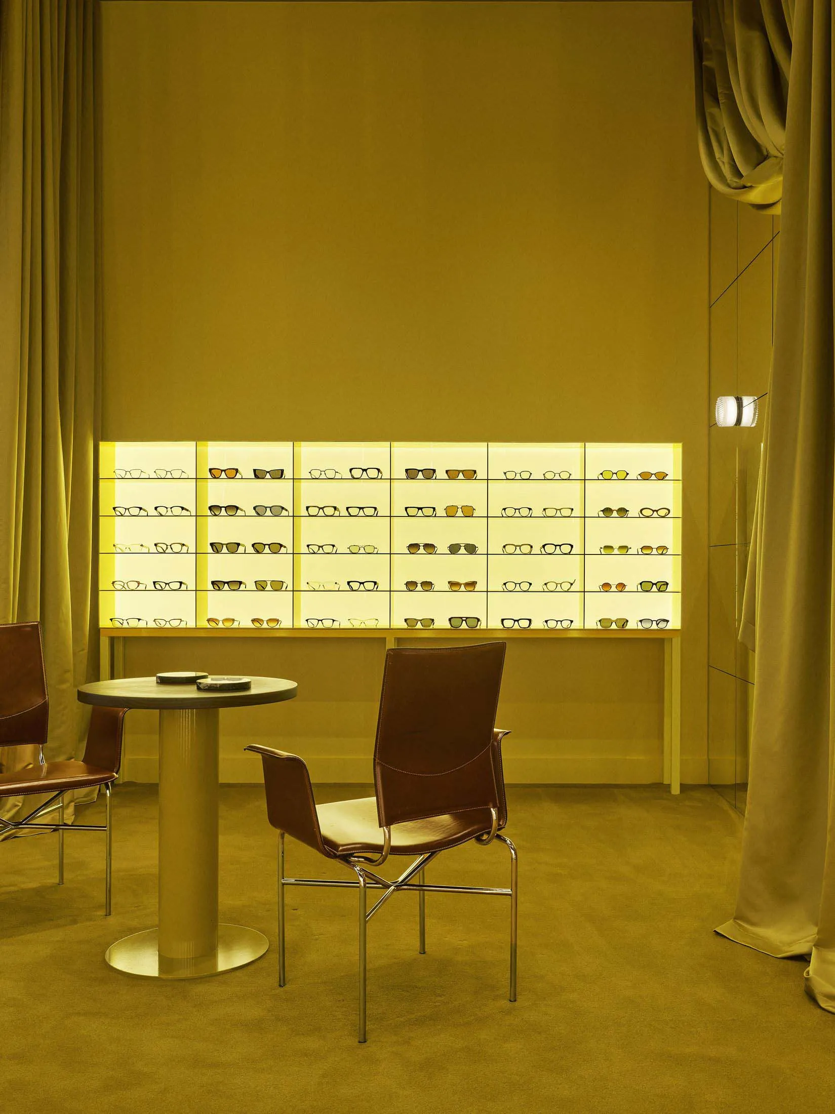 A store or showroom with a yellow wall and a display case filled with various pairs of glasses, arranged in an organized and visually appealing presentation