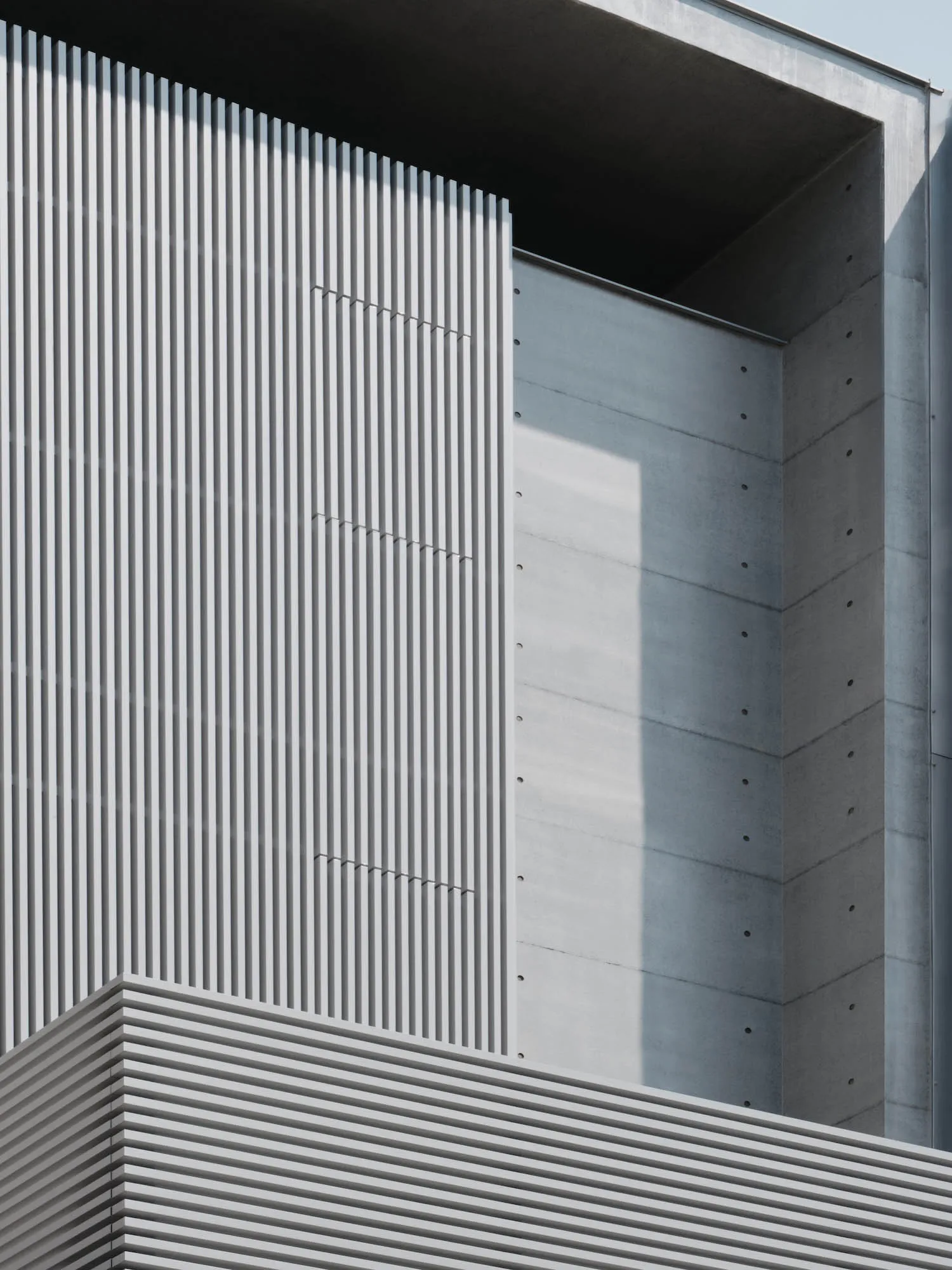 A modern building with a large concrete wall featuring a row of vertical stripes, set against a bright and sunny day