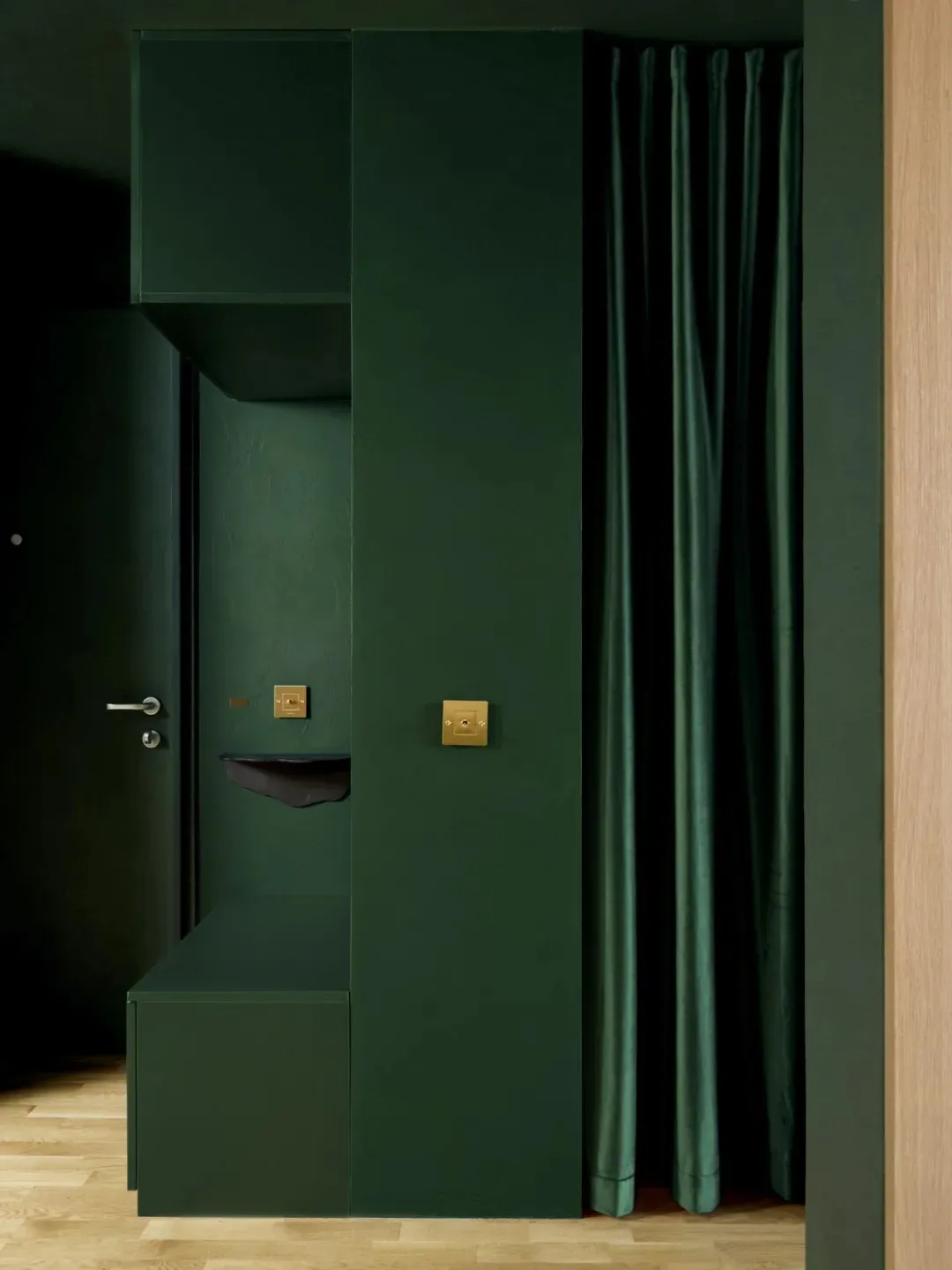 A small, dark room with green walls and a green door, featuring a simple and minimalistic design with a green curtain and a closet or storage area
