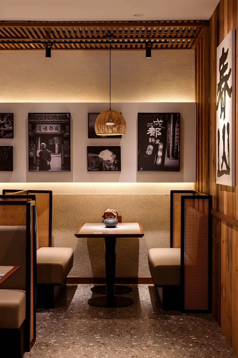 A modern restaurant with a dining table and chairs, surrounded by pictures on the wall, and a wooden floor, lit by a hanging light
