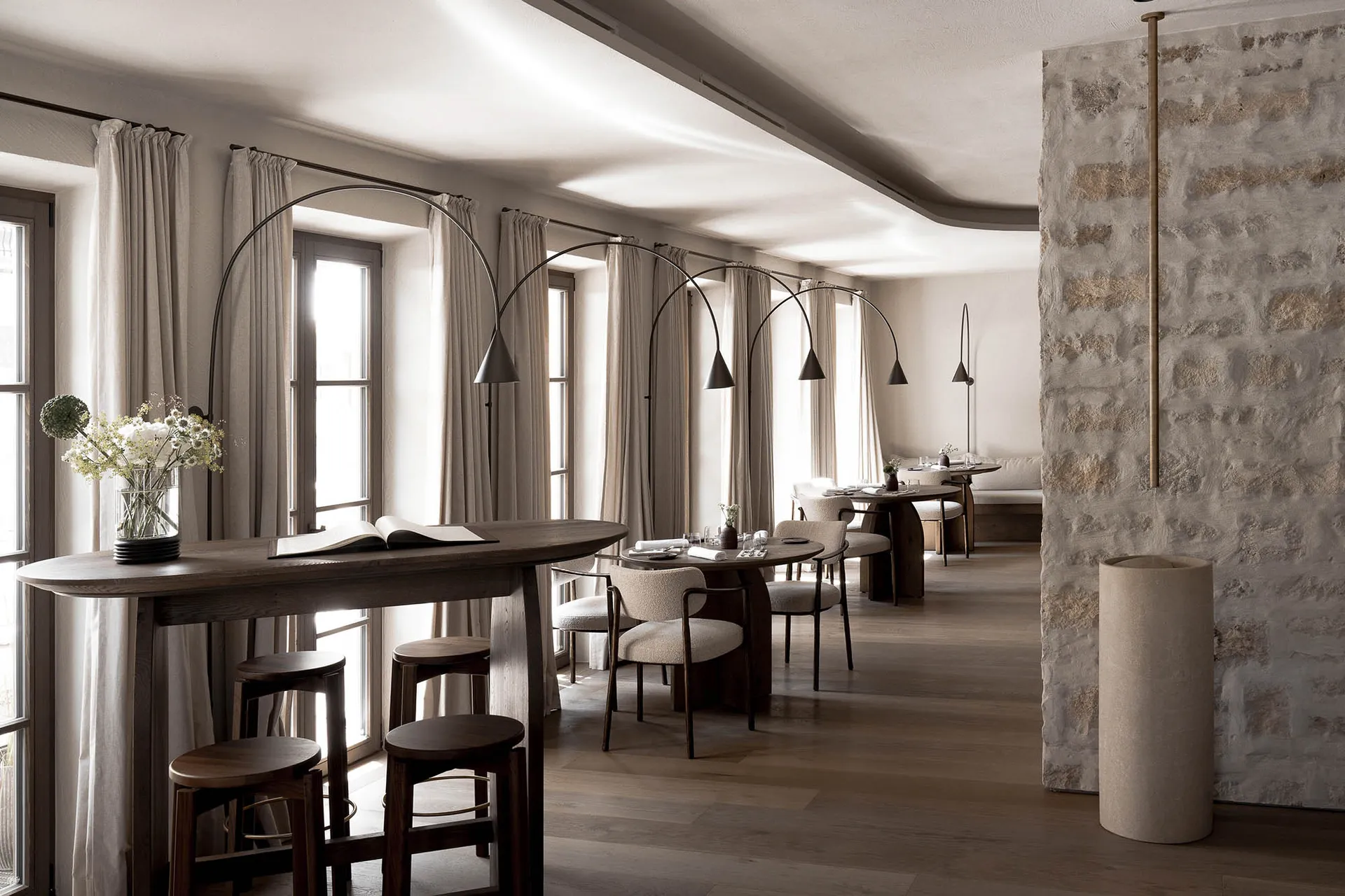A well-lit restaurant interior with a long wooden table and multiple chairs, surrounded by additional seating and wooden furnishings
