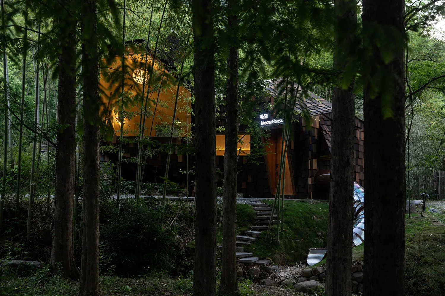 A modern house with a wooden exterior, surrounded by trees, featuring a large window and a door, with soft and diffused lighting creating a peaceful atmosphere