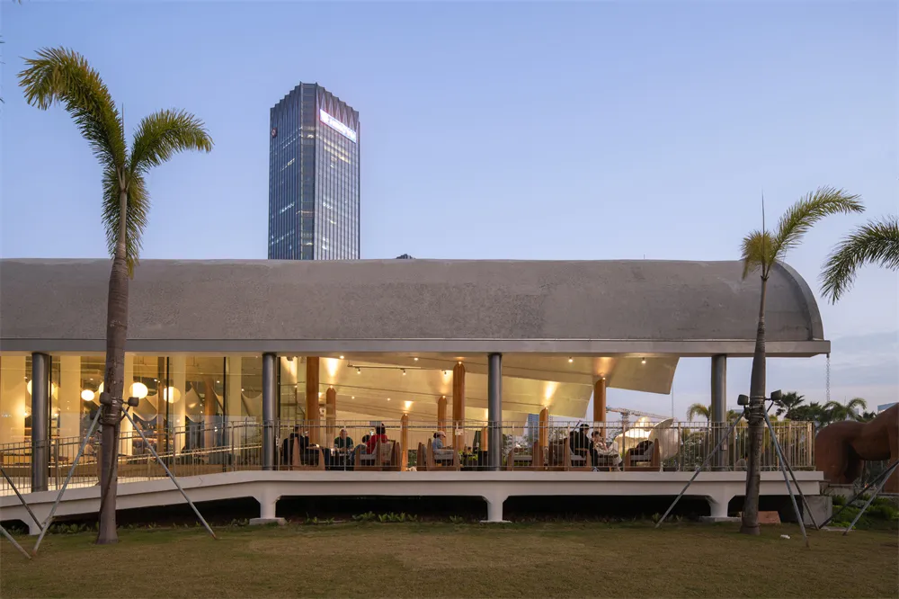 A modern restaurant with wooden dining tables and chairs, set against a backdrop of a tall skyscraper, with soft and warm lighting creating a sophisticated atmosphere