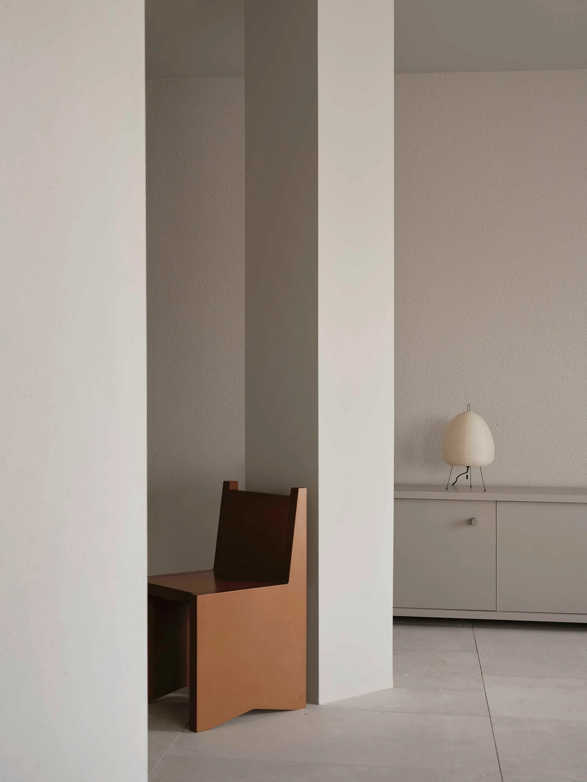 A small room with a white wall, a brown wooden chair in the corner, and a gray color scheme, with a small table nearby