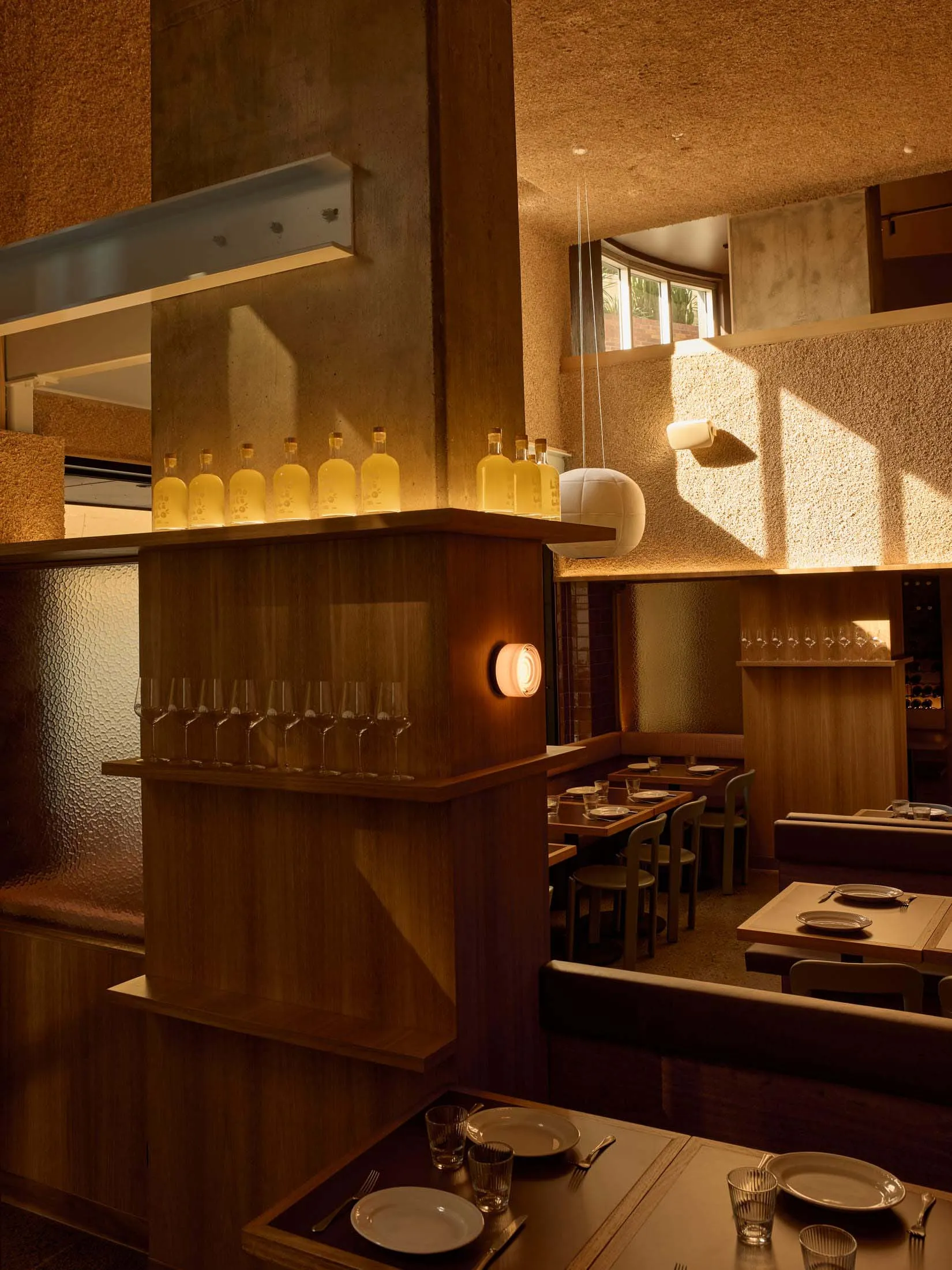 A modern restaurant with a semi-circular seating area, a bar with bottles, and a mix of wood and concrete walls, lit dimly for a cozy atmosphere