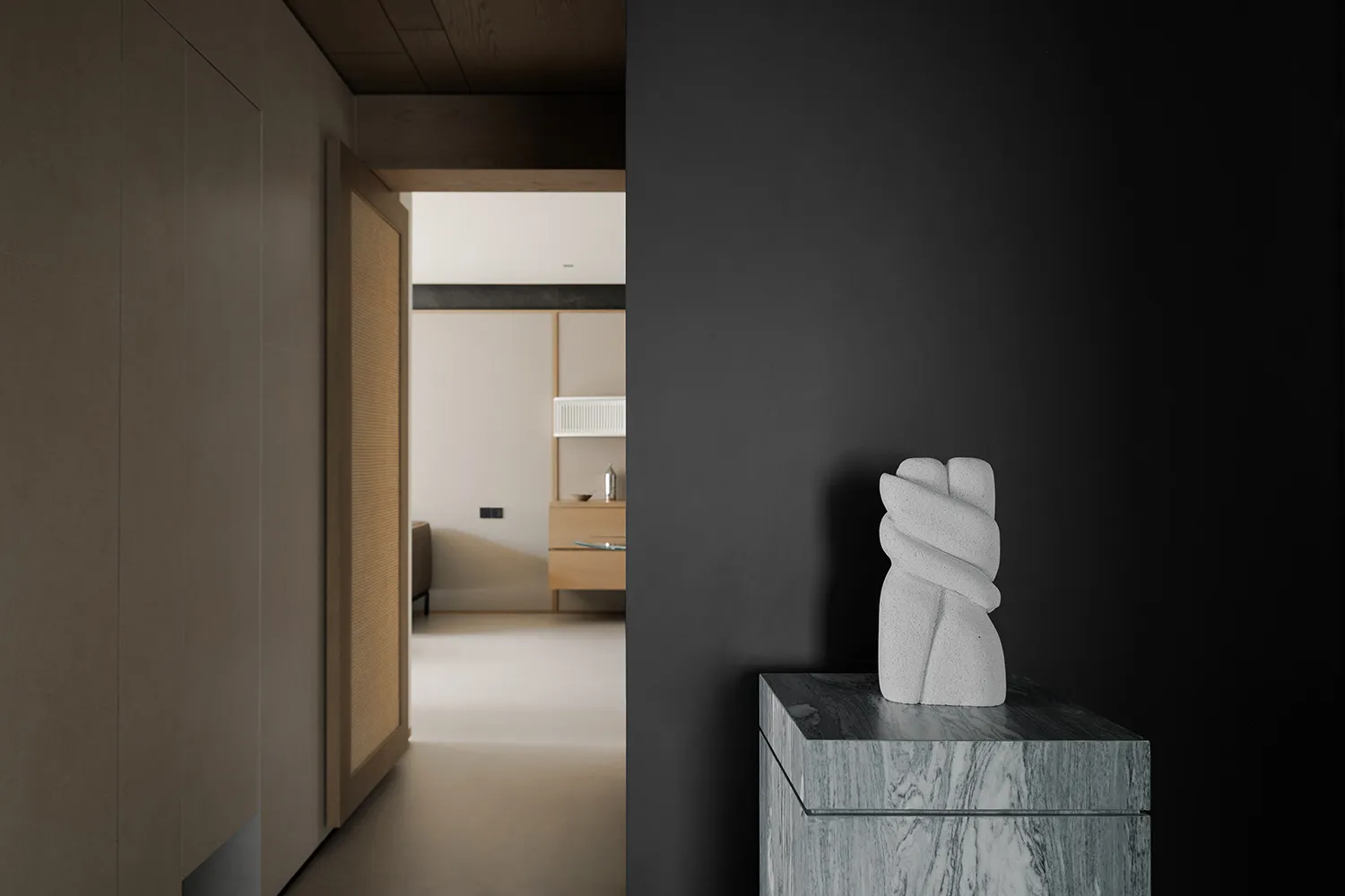 A black and white living room with a stone pedestal, a white sculpture of a hand, a couch, and a dining table, in a modern and minimalist style