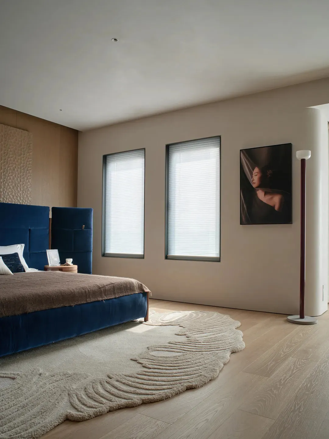A well-lit bedroom with a bed, chair, and painting, featuring predominantly wooden materials and a comfortable atmosphere