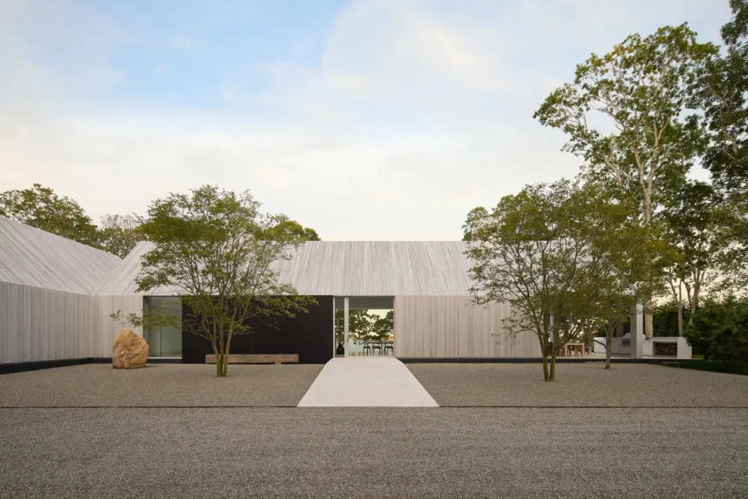 A modern house with a wooden exterior, large window, and door, surrounded by trees in a residential area