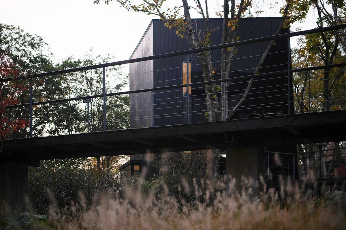 A calm and serene black and white photograph of a house with a metal deck and a black roof, taken from a low angle looking up at the structure