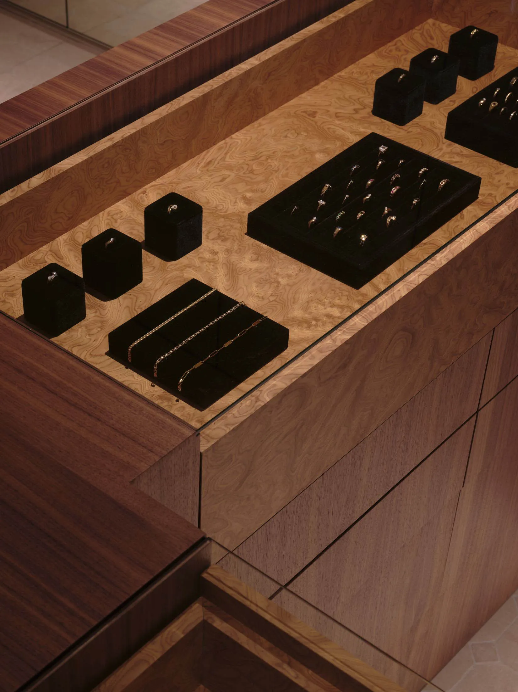 A wooden cabinet with a drawer and shelf, containing organized rings, bracelets, and a watch, set against a natural light background