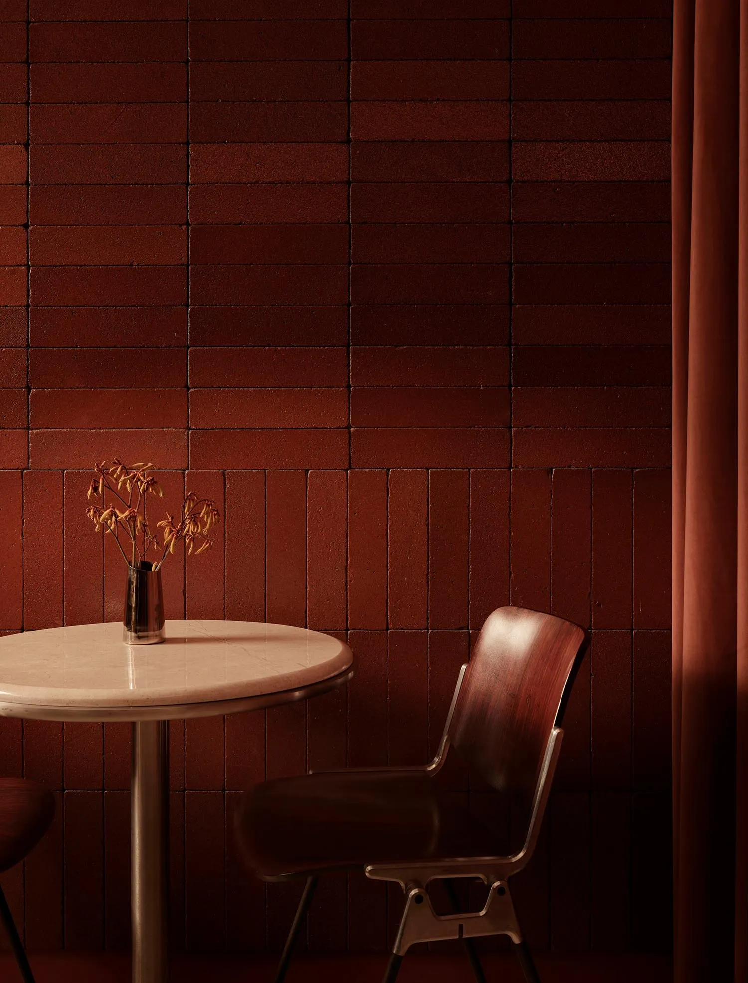 Dining area with a marble table and wooden chairs, surrounded by a brick wall, with a vase and flowers on the table, in a dimly lit space