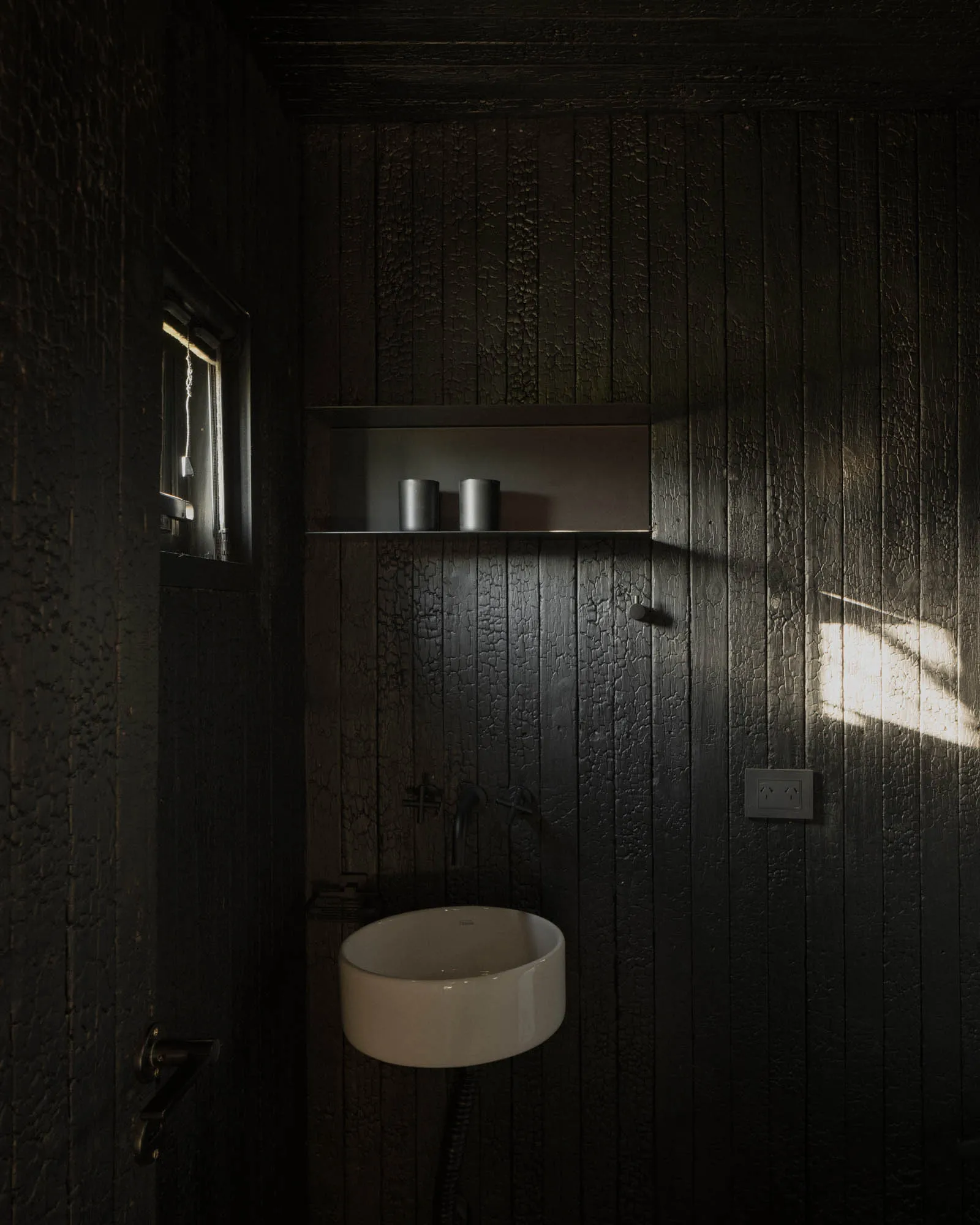 Dimly lit vintage bathroom with a sink, mirror, and window, featuring wooden walls
