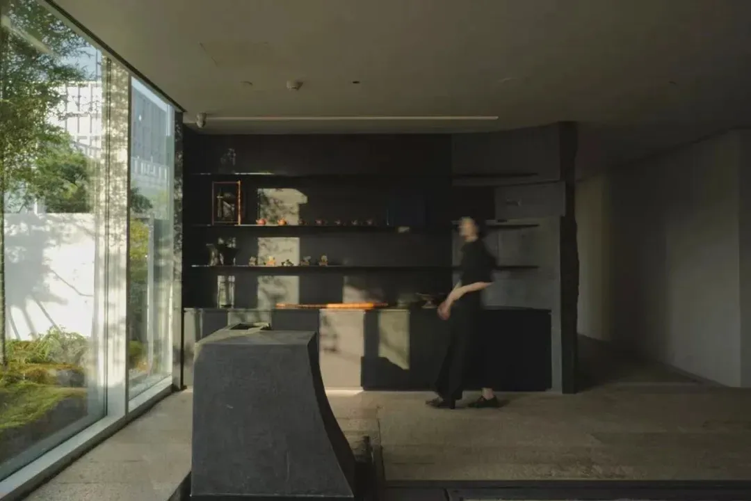 A woman walks towards a counter in a calm and inviting dining area with a black and white color scheme and a window in the background