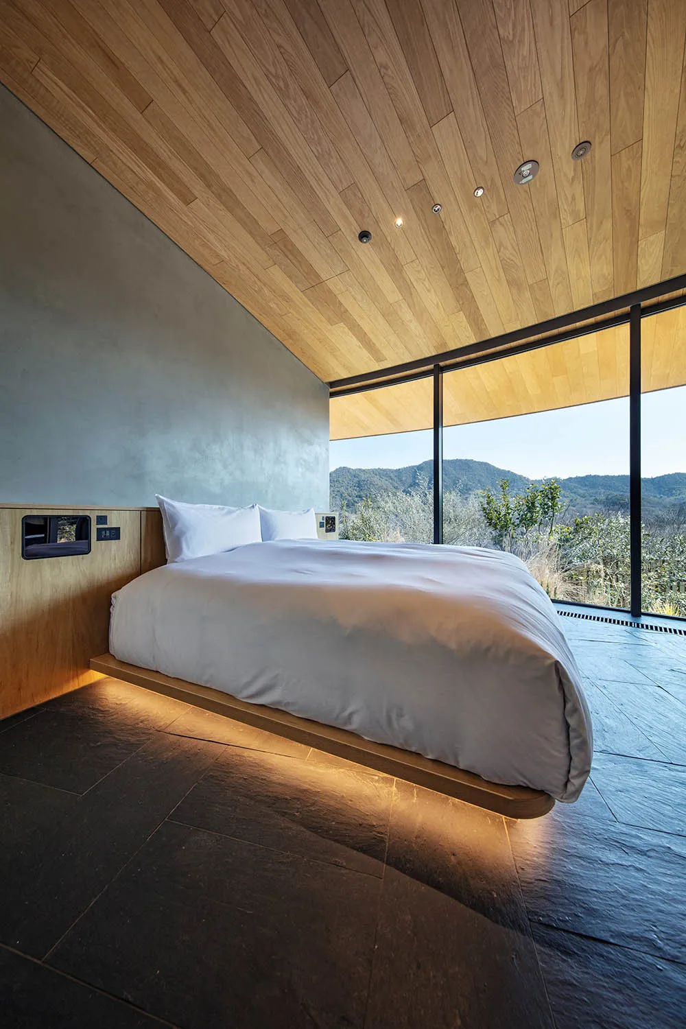 A well-lit modern bedroom with a large bed, wooden floor, and white comforter, creating a warm and inviting atmosphere