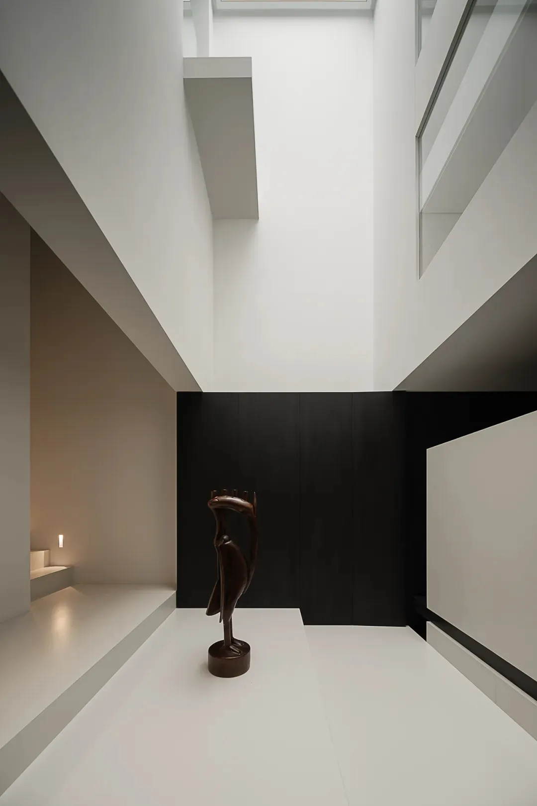 A black and white photograph of a bird sculpture on a white pedestal in a minimalist room with a black and white color scheme