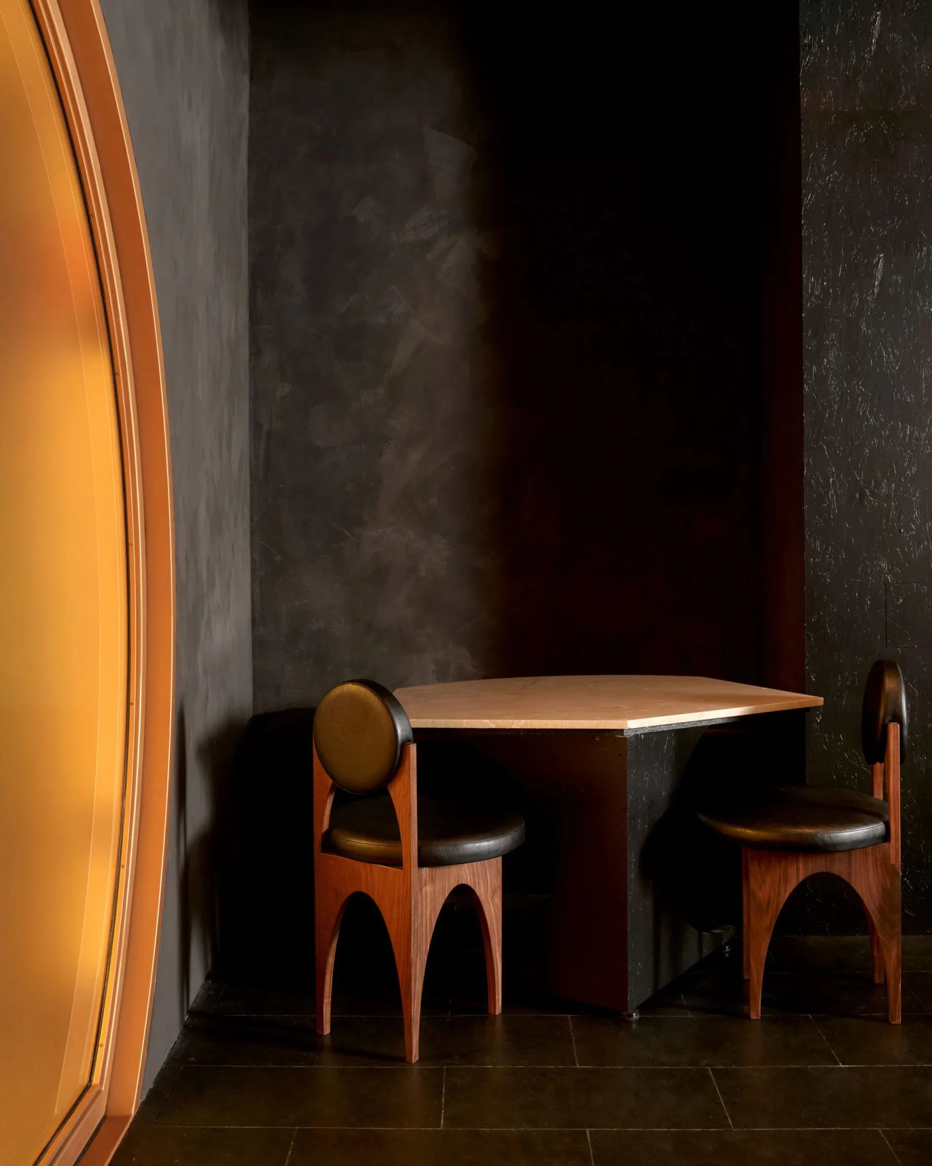 A dimly lit dining area with a wooden table and chairs, surrounded by additional seating options and a black and brown color scheme