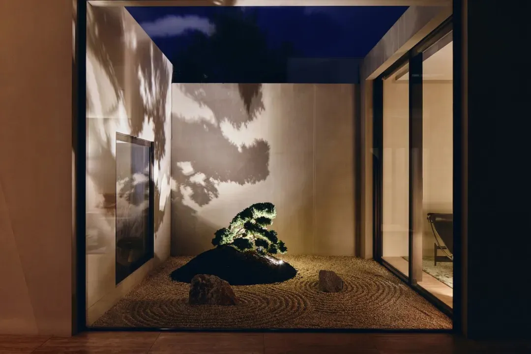 A cozy living room with a small potted bonsai tree surrounded by rocks, a couch, and a chair, creating a warm and inviting atmosphere
