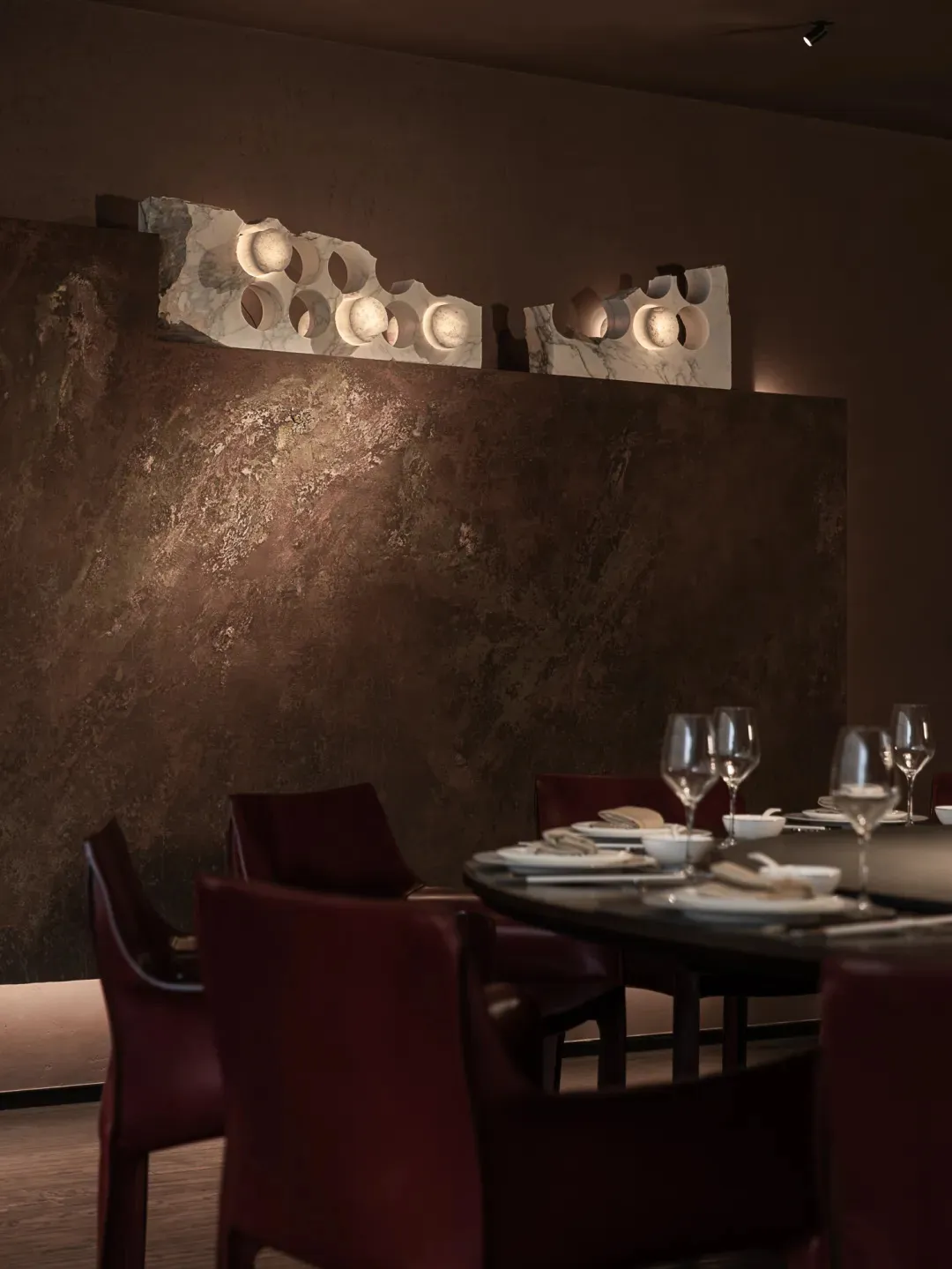 Elegant dining room with a marble wall, a stone wall, a dining table, chairs, wine glasses, a vase, and a bowl