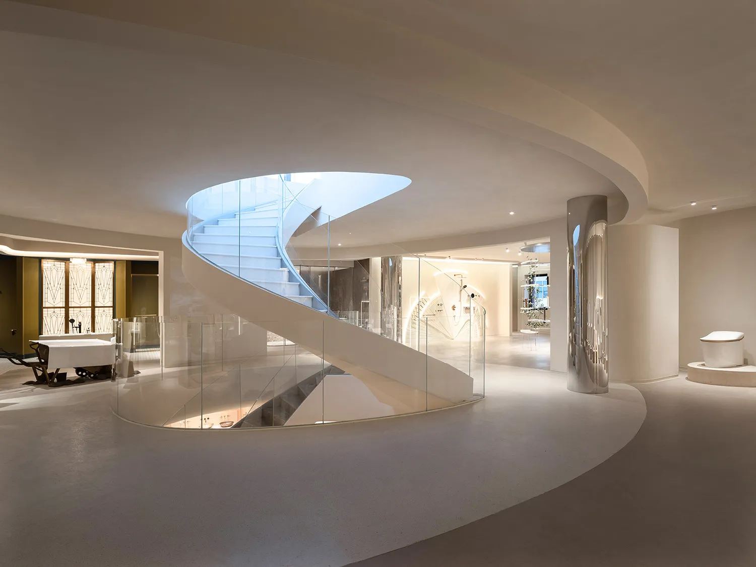 A modern, white, circular building with a glass spiral staircase, blending living and dining areas, with a dining table and sleek, open design