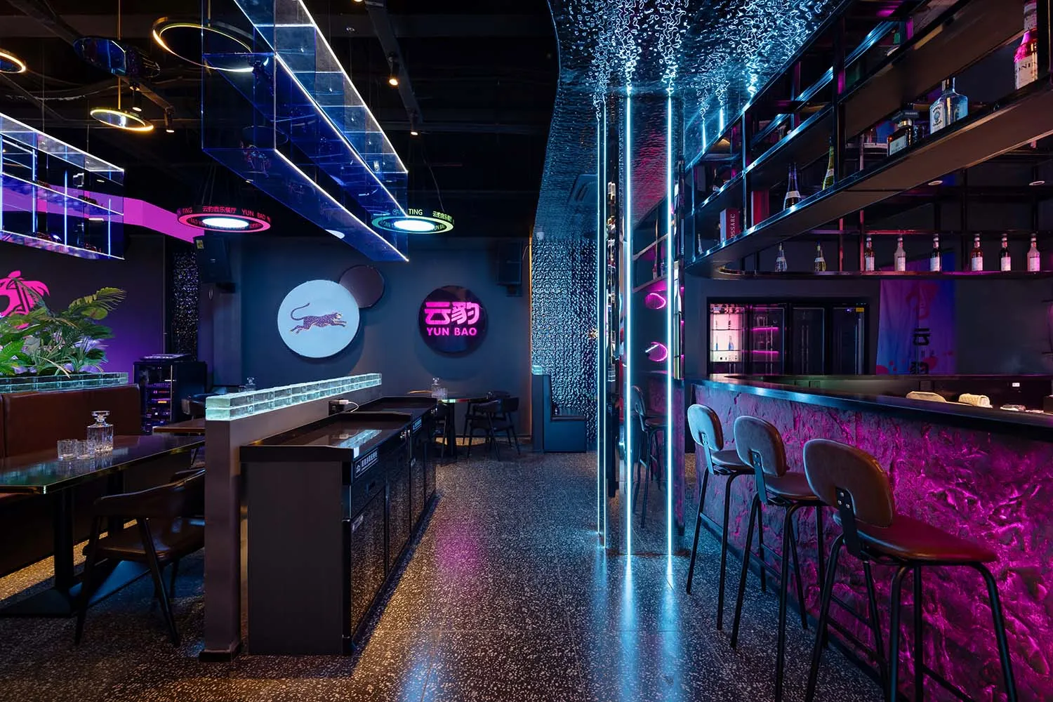A modern bar with a black counter and pink floor, surrounded by chairs and a dining table in a dimly lit environment