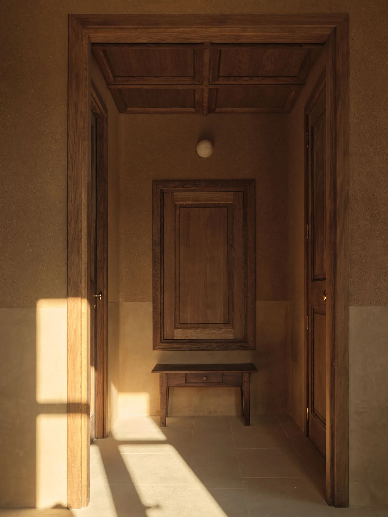 A small room with a wooden bench against the wall, a wooden door, and a window letting in natural light