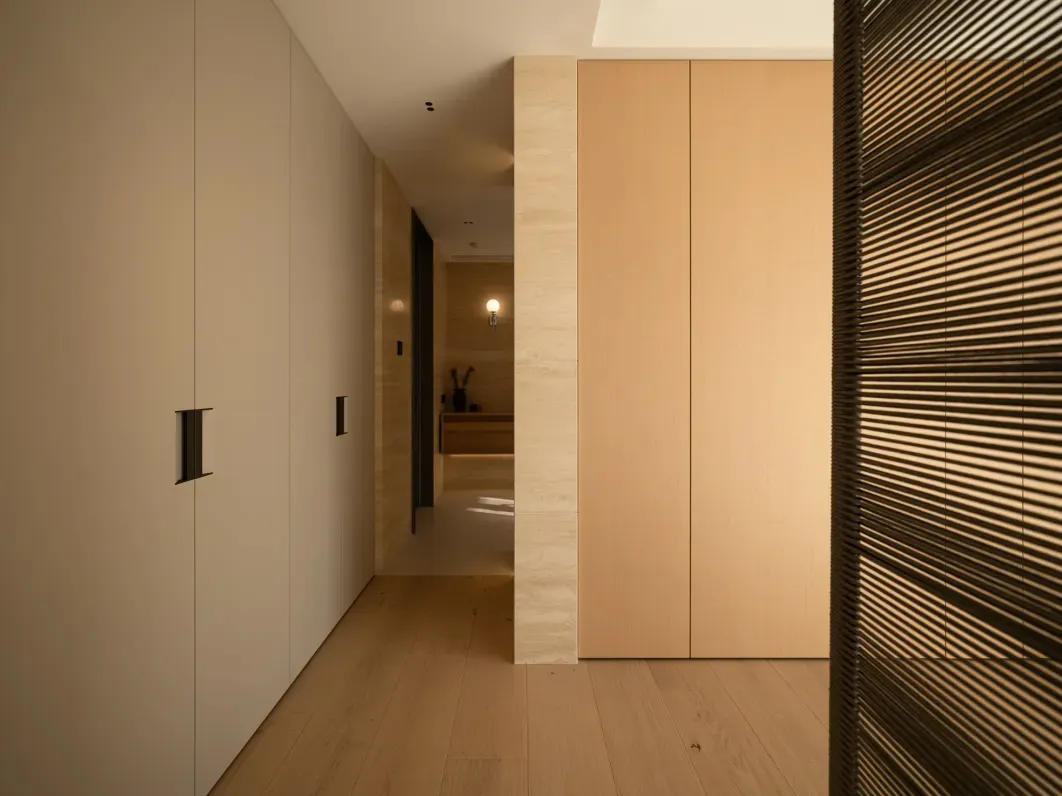 Well-lit hallway with a wooden floor, a door, and a glimpse of a room beyond