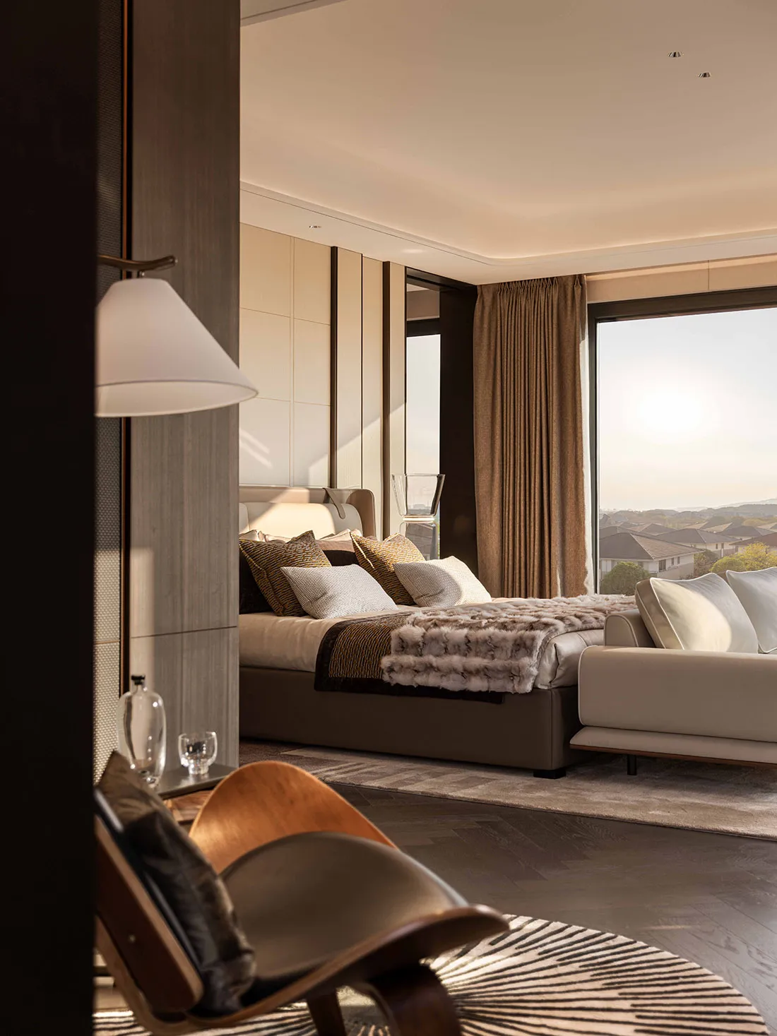 Cozy bedroom with a brown headboard, a chair, and a couch, lit by natural light from a large window