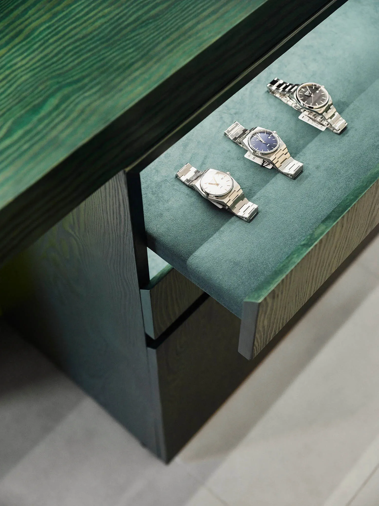 A wooden desk with a drawer and a display of silver and blue watches on a well-lit living space