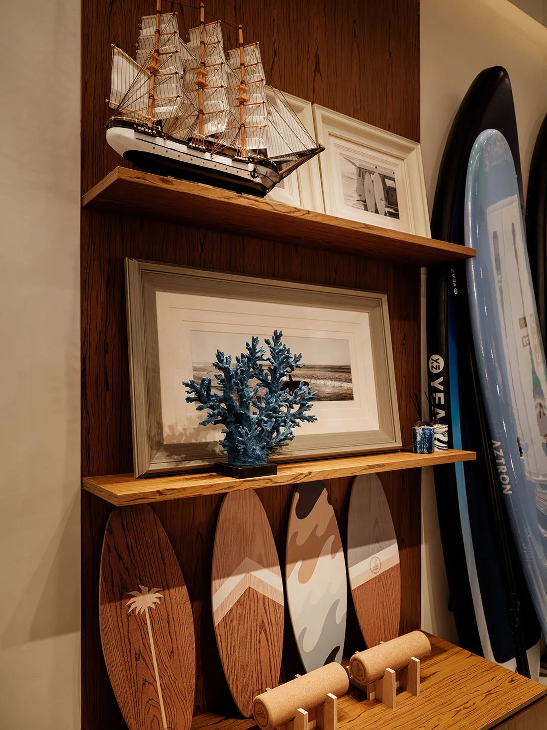 Cozy living space with a wooden shelf displaying surfboards, framed pictures, and a plant, suggesting a relaxed coastal atmosphere