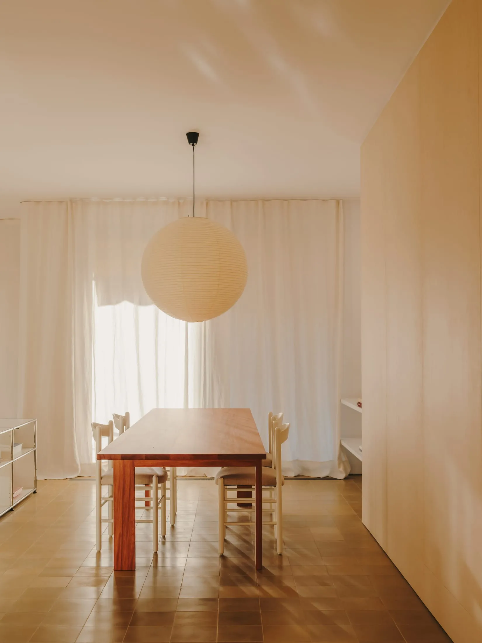 Dining room with a wooden table and chairs, surrounded by a modern and minimalistic space with natural light and a warm atmosphere