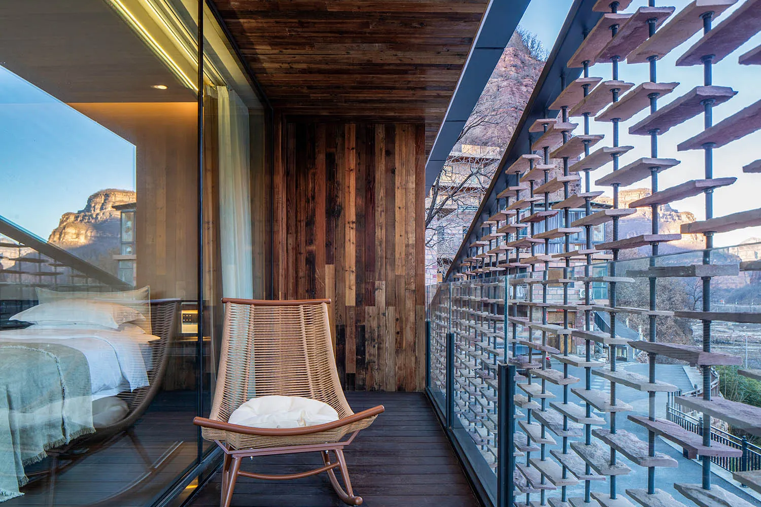 A wooden chair on a wooden deck near a glass wall offering a view of the surrounding area, with a daytime atmosphere of relaxation and comfort
