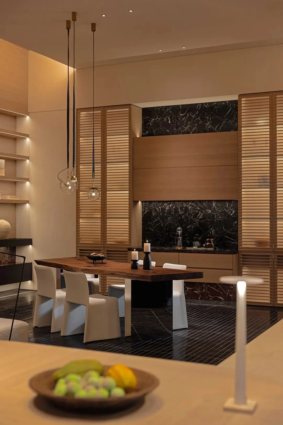 A well-lit modern kitchen with a wooden dining table, white chairs, and a marble countertop, creating a warm and inviting atmosphere