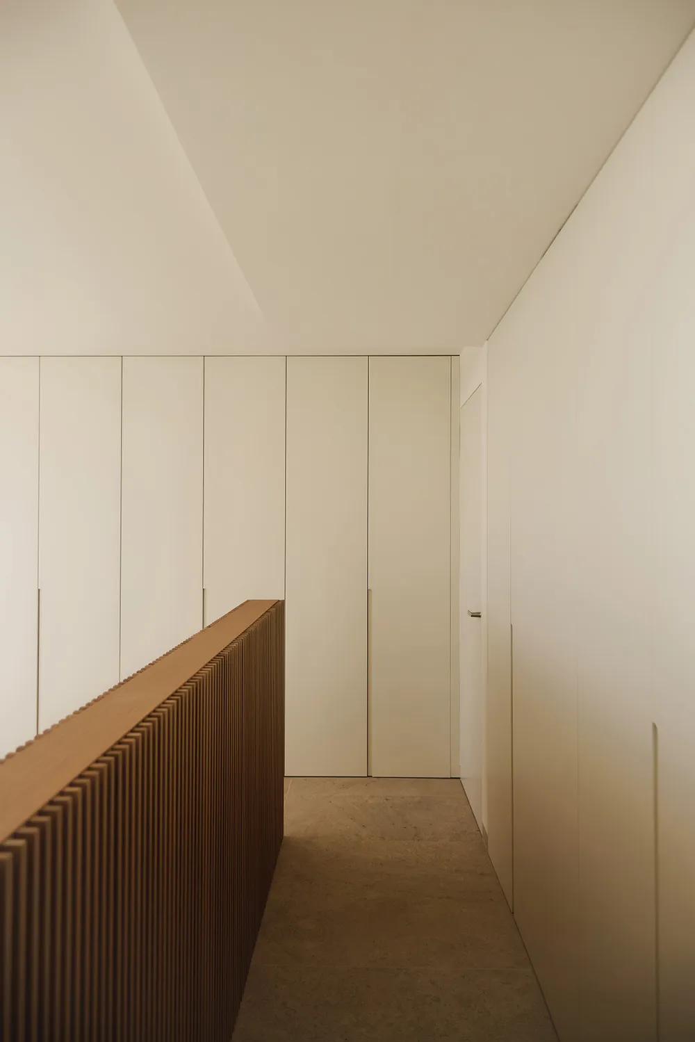 A clean and well-lit white hallway with a brown wooden bench along the wall